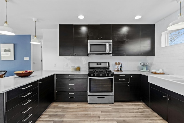 kitchen with dark cabinetry, a peninsula, decorative backsplash, light countertops, and appliances with stainless steel finishes