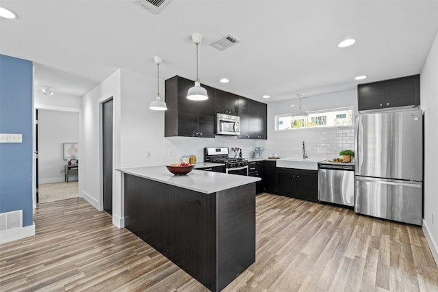 kitchen featuring visible vents, a peninsula, light wood-style floors, stainless steel appliances, and dark cabinets