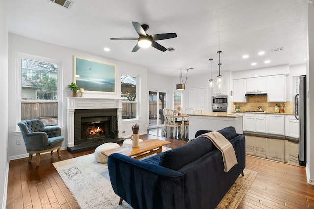 living room with a brick fireplace, ceiling fan, and light wood-type flooring