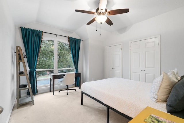 carpeted bedroom featuring multiple closets, vaulted ceiling, and ceiling fan