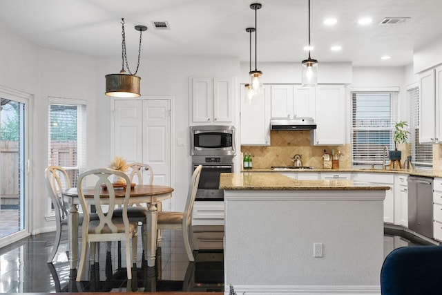 kitchen with a center island, pendant lighting, stainless steel appliances, light stone countertops, and white cabinets