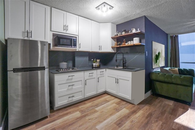 kitchen with sink, backsplash, white cabinets, light hardwood / wood-style floors, and stainless steel appliances