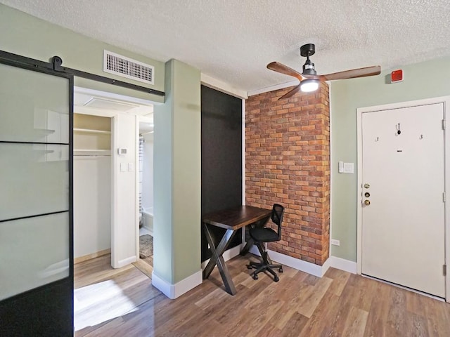 office area with ceiling fan, a barn door, a textured ceiling, and light wood-type flooring