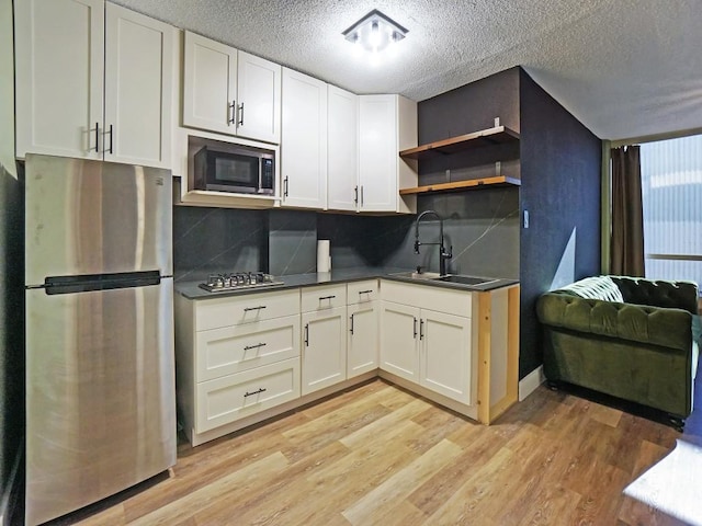 kitchen with appliances with stainless steel finishes, sink, backsplash, and light hardwood / wood-style floors