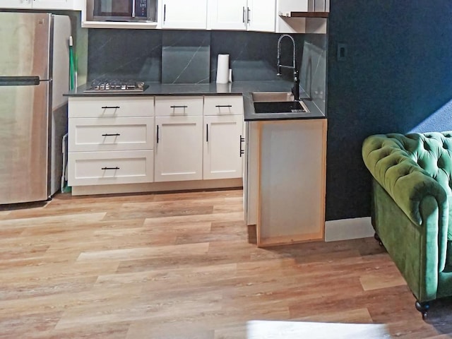 kitchen featuring sink, appliances with stainless steel finishes, white cabinetry, backsplash, and light hardwood / wood-style floors