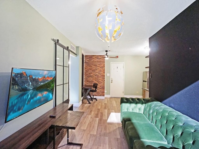 living room featuring ceiling fan with notable chandelier, light hardwood / wood-style floors, and a barn door