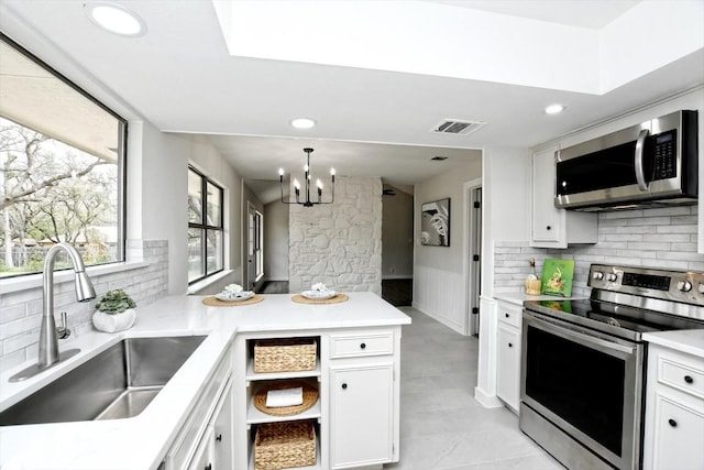 kitchen featuring sink, backsplash, stainless steel appliances, white cabinets, and decorative light fixtures