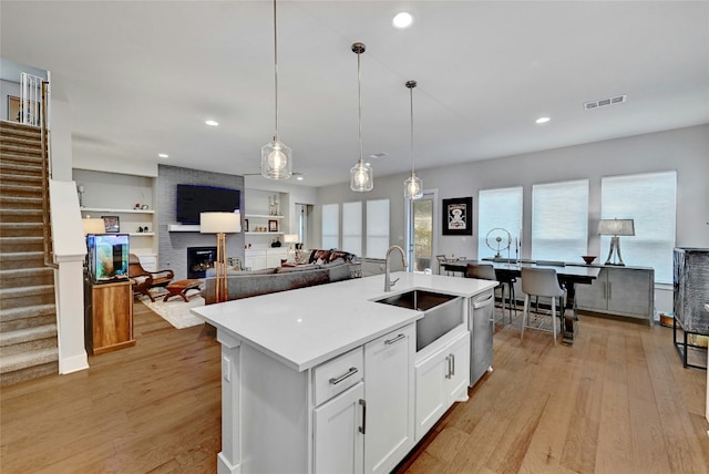 kitchen featuring sink, white cabinetry, a kitchen island with sink, hanging light fixtures, and a brick fireplace