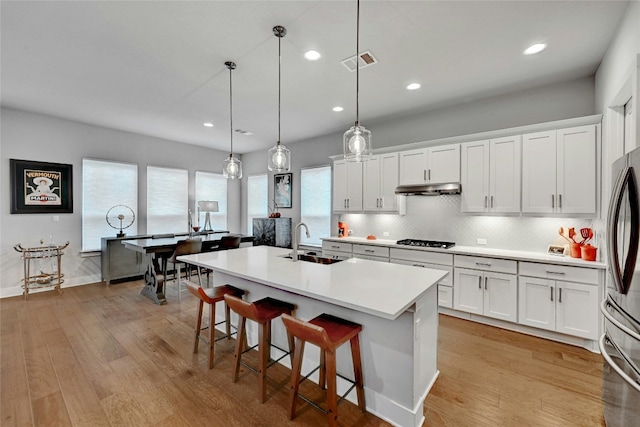 kitchen with decorative light fixtures, white cabinetry, sink, a kitchen island with sink, and gas cooktop