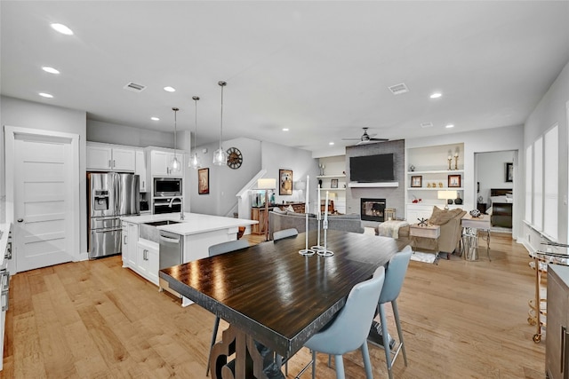 dining area featuring built in shelves, sink, light hardwood / wood-style flooring, ceiling fan, and a fireplace