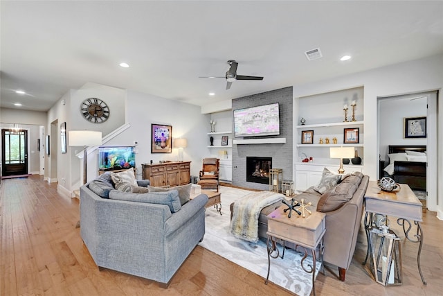 living room featuring ceiling fan, light wood-type flooring, a fireplace, and built in shelves