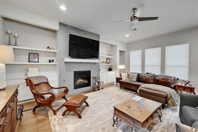 living room featuring ceiling fan, built in features, a brick fireplace, and light wood-type flooring