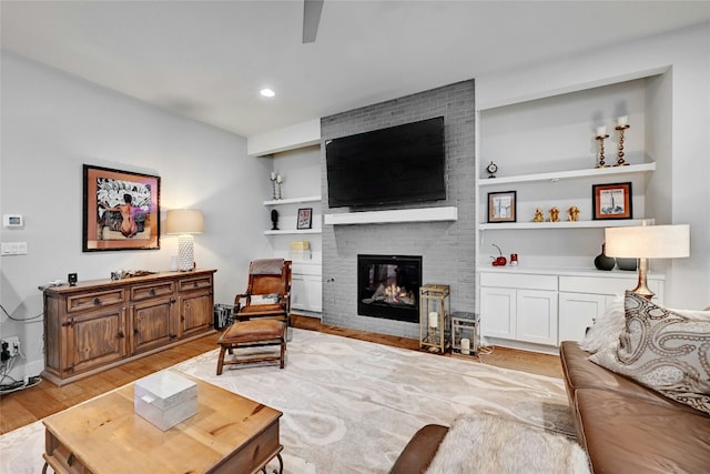 living room with built in features, a fireplace, and light hardwood / wood-style flooring