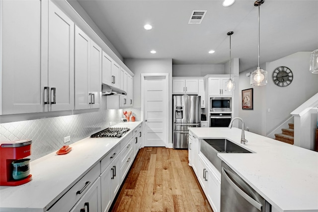 kitchen featuring sink, appliances with stainless steel finishes, white cabinetry, an island with sink, and decorative light fixtures