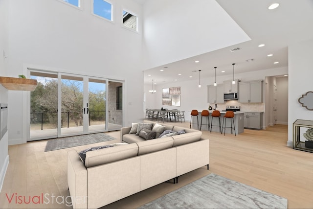 living room with a notable chandelier, a towering ceiling, light hardwood / wood-style floors, and french doors