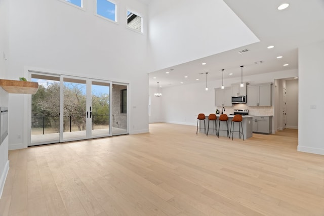 unfurnished living room featuring a towering ceiling, a chandelier, and light wood-type flooring