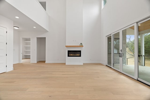 unfurnished living room featuring french doors, built in shelves, a high ceiling, and light wood-type flooring