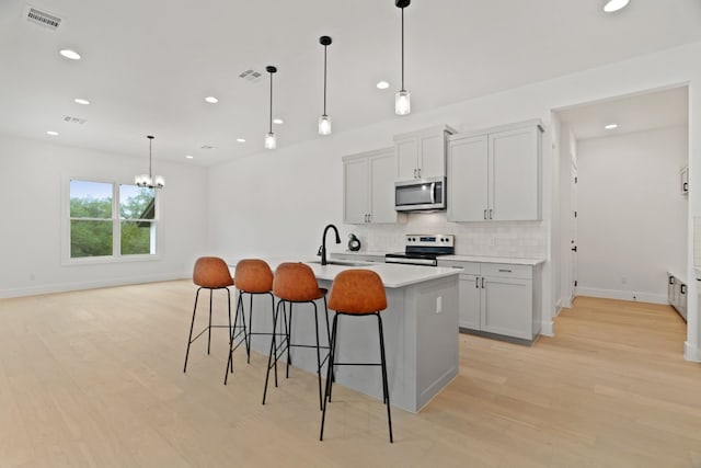 kitchen with sink, decorative light fixtures, appliances with stainless steel finishes, an island with sink, and decorative backsplash