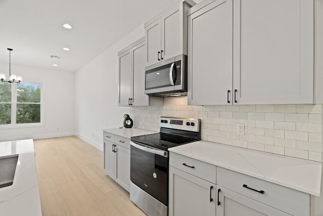 kitchen with pendant lighting, tasteful backsplash, appliances with stainless steel finishes, and light stone counters