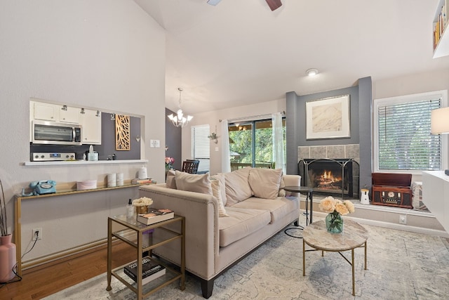 living room with a notable chandelier, vaulted ceiling, a tile fireplace, and light hardwood / wood-style flooring