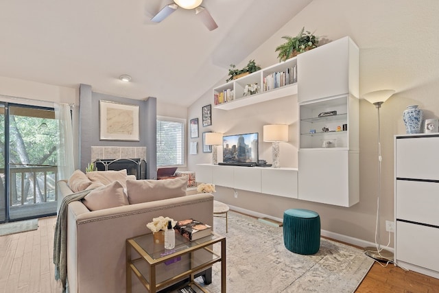 living room featuring vaulted ceiling, ceiling fan, a tiled fireplace, and light hardwood / wood-style floors