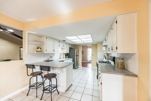 kitchen with light tile patterned flooring, range with gas cooktop, white cabinetry, stainless steel refrigerator, and kitchen peninsula