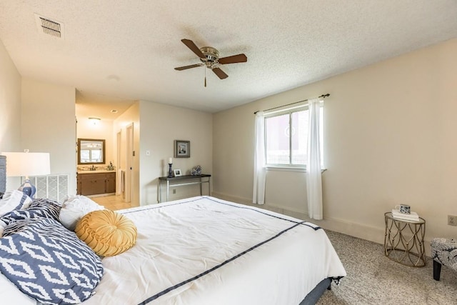 carpeted bedroom with ensuite bathroom, ceiling fan, and a textured ceiling