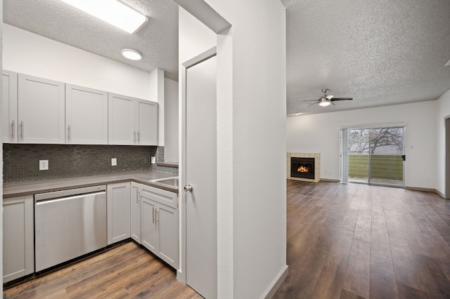 kitchen featuring hardwood / wood-style flooring, tasteful backsplash, white cabinets, a tiled fireplace, and stainless steel dishwasher