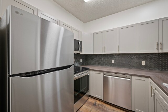 kitchen with butcher block counters, tasteful backsplash, a textured ceiling, appliances with stainless steel finishes, and dark hardwood / wood-style floors