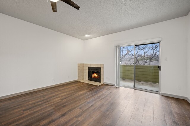 unfurnished living room featuring a tiled fireplace, ceiling fan, a textured ceiling, and dark hardwood / wood-style flooring