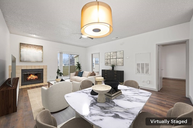 dining room featuring dark hardwood / wood-style flooring, a tile fireplace, and a textured ceiling