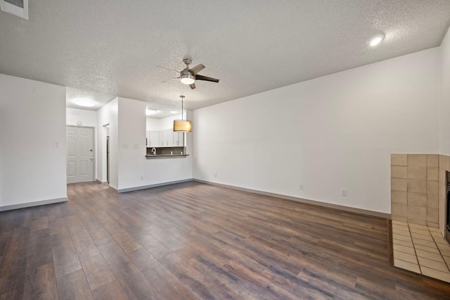 unfurnished living room featuring a tile fireplace, dark wood-type flooring, a textured ceiling, and ceiling fan