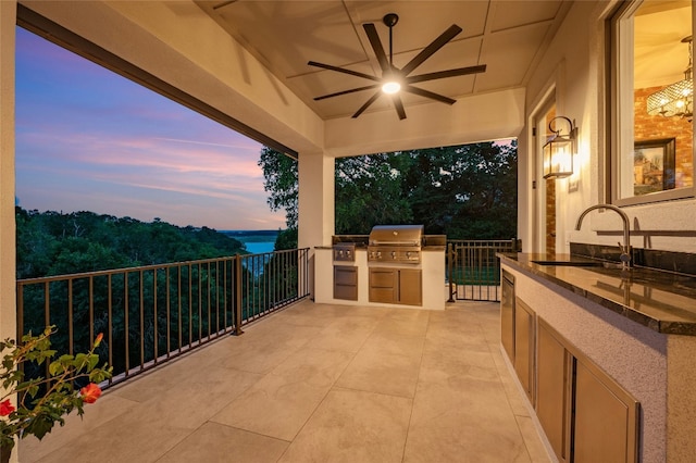 patio terrace at dusk featuring an outdoor kitchen, sink, a water view, grilling area, and ceiling fan