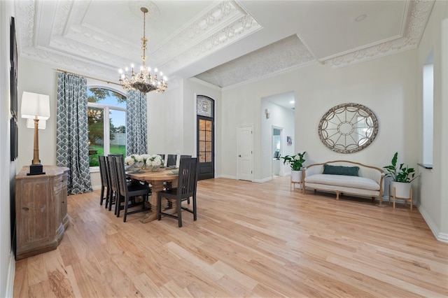 dining space with a towering ceiling, a chandelier, light hardwood / wood-style floors, a raised ceiling, and crown molding