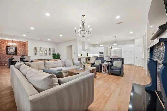 living room with brick wall, a fireplace, a chandelier, and light hardwood / wood-style flooring