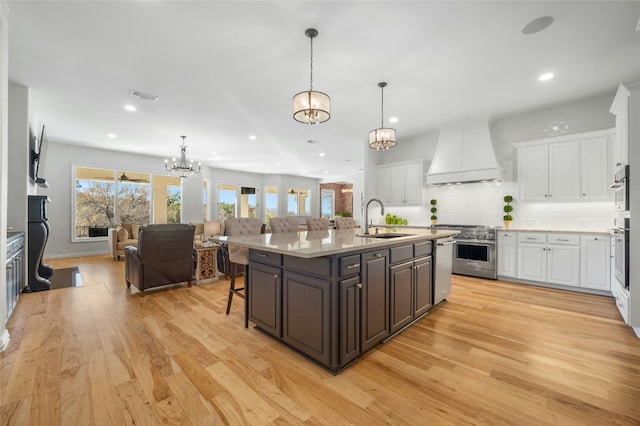 kitchen featuring white cabinetry, sink, custom exhaust hood, a kitchen island with sink, and stainless steel appliances