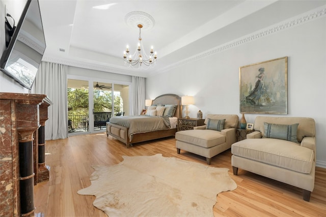 bedroom with access to exterior, a tray ceiling, light hardwood / wood-style flooring, and a notable chandelier