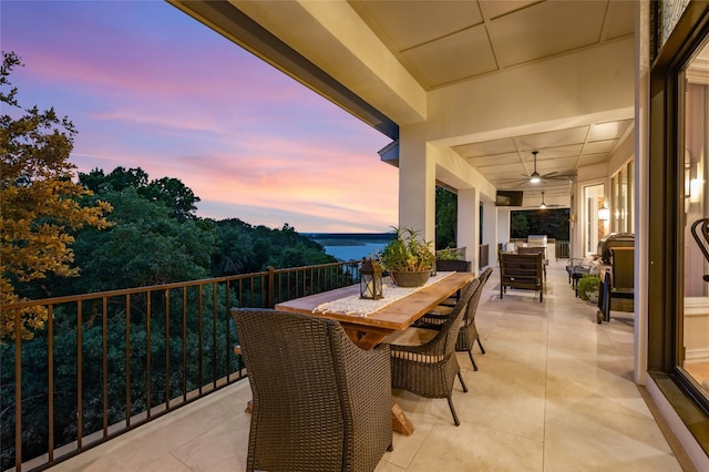 balcony at dusk featuring a water view and ceiling fan