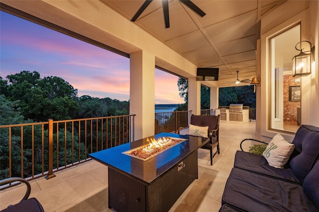 patio terrace at dusk featuring area for grilling, a fire pit, and ceiling fan