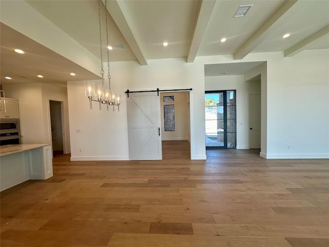 interior space with beamed ceiling, a barn door, and light wood-type flooring