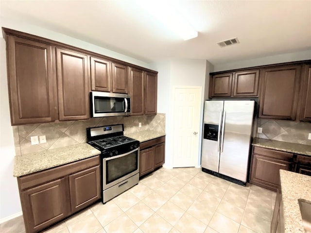 kitchen with stainless steel appliances, light stone countertops, dark brown cabinets, and decorative backsplash