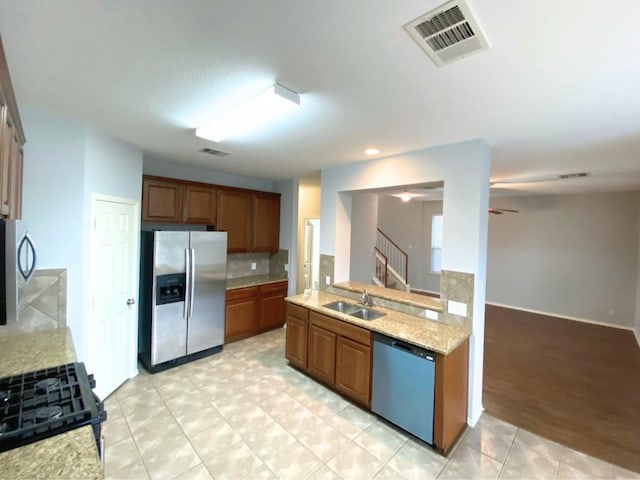 kitchen featuring sink, appliances with stainless steel finishes, tasteful backsplash, light stone counters, and kitchen peninsula