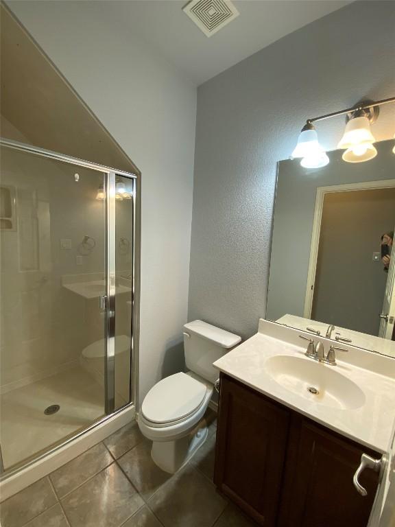 bathroom with tile patterned flooring, vanity, a shower with shower door, and toilet