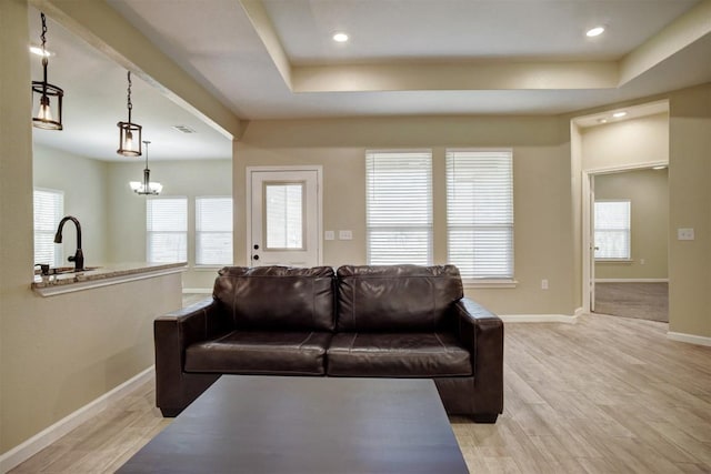 living room featuring a tray ceiling, a chandelier, sink, and light wood-type flooring