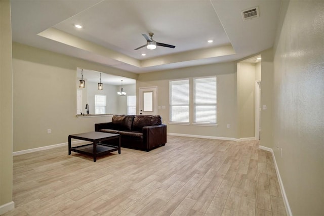 living room featuring light hardwood / wood-style flooring, ceiling fan, and a tray ceiling