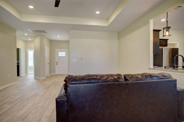 living room with sink, light hardwood / wood-style flooring, and a raised ceiling