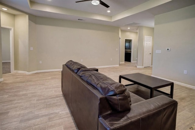 living room featuring light hardwood / wood-style flooring, ceiling fan, and a tray ceiling