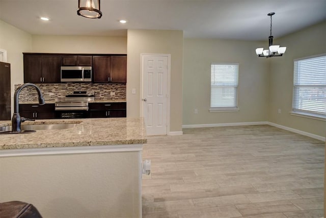 kitchen featuring dark brown cabinetry, sink, light stone counters, appliances with stainless steel finishes, and pendant lighting