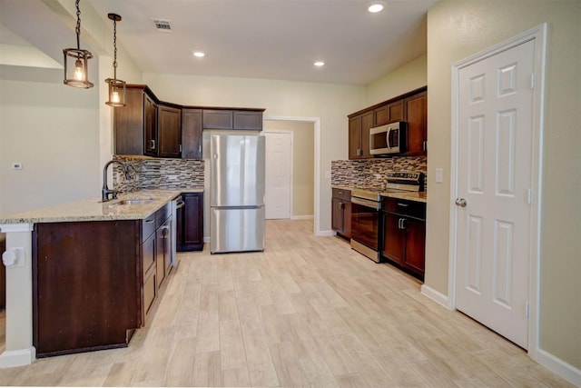 kitchen with pendant lighting, sink, stainless steel appliances, dark brown cabinetry, and light wood-type flooring