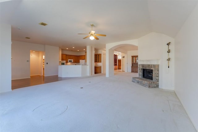 unfurnished living room featuring a brick fireplace, light colored carpet, and ceiling fan